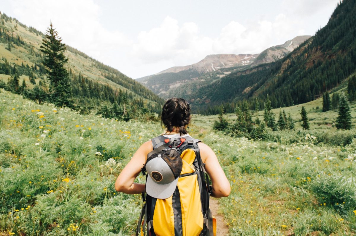 A woman heads onto a wildflower-filled and tree-lined hiking trail